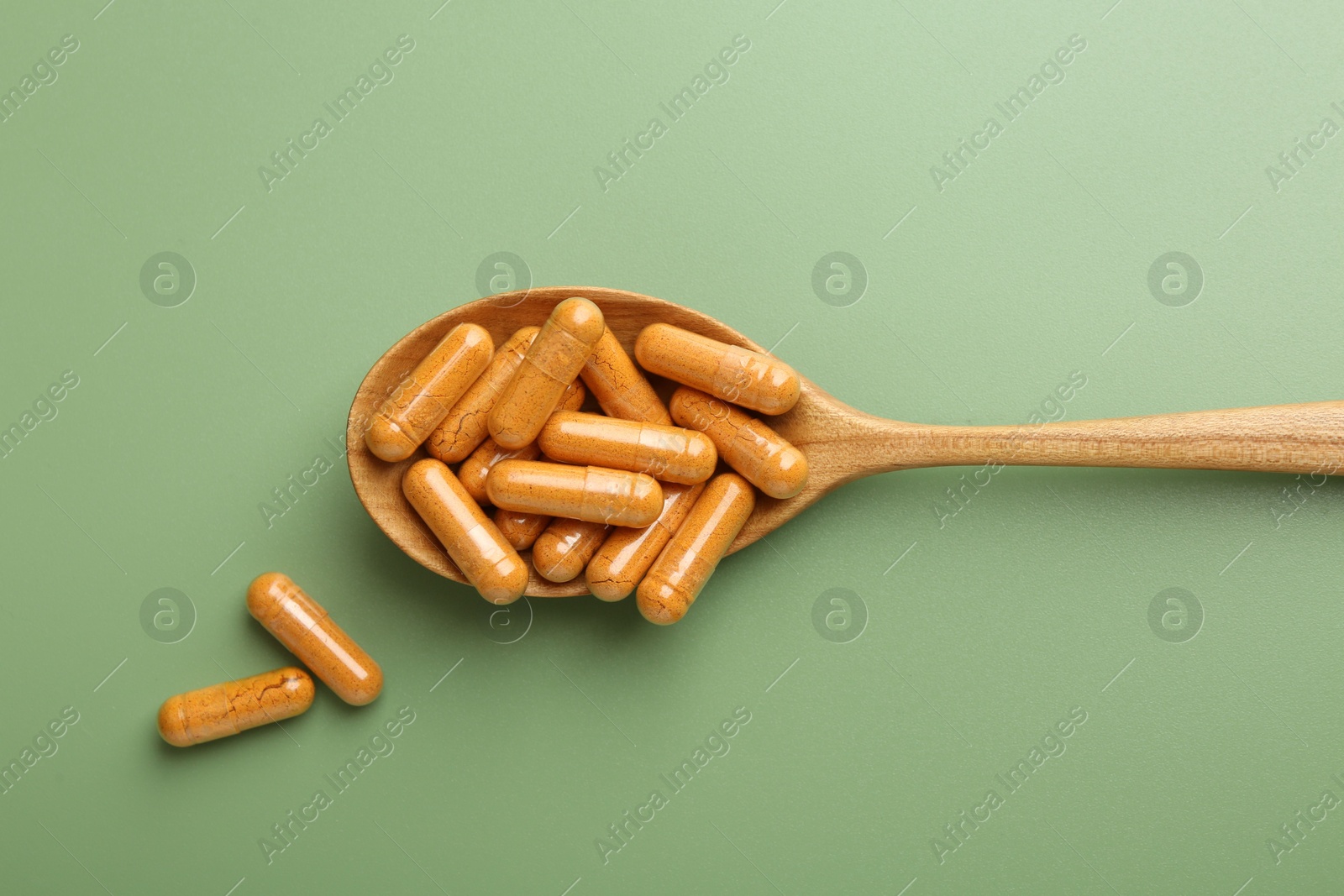 Photo of Turmeric capsules in spoon on light green background, top view