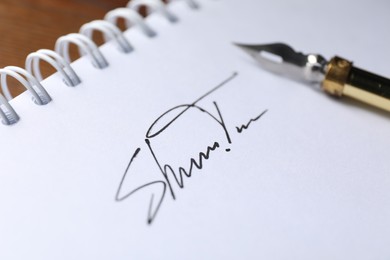 Photo of Notepad with signature and fountain pen on table, closeup