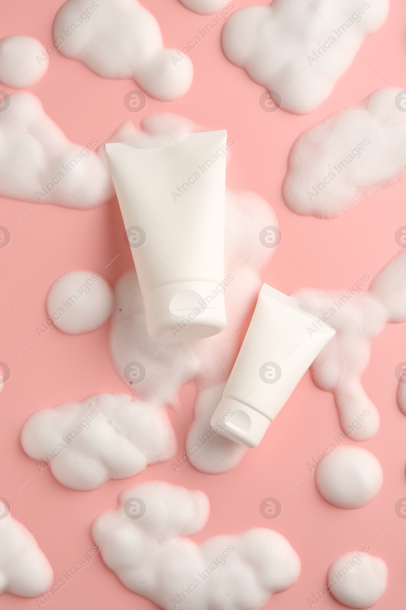 Photo of Tubes of cosmetic products with foam on pink background, top view