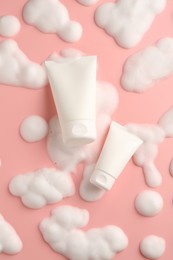 Tubes of cosmetic products with foam on pink background, top view