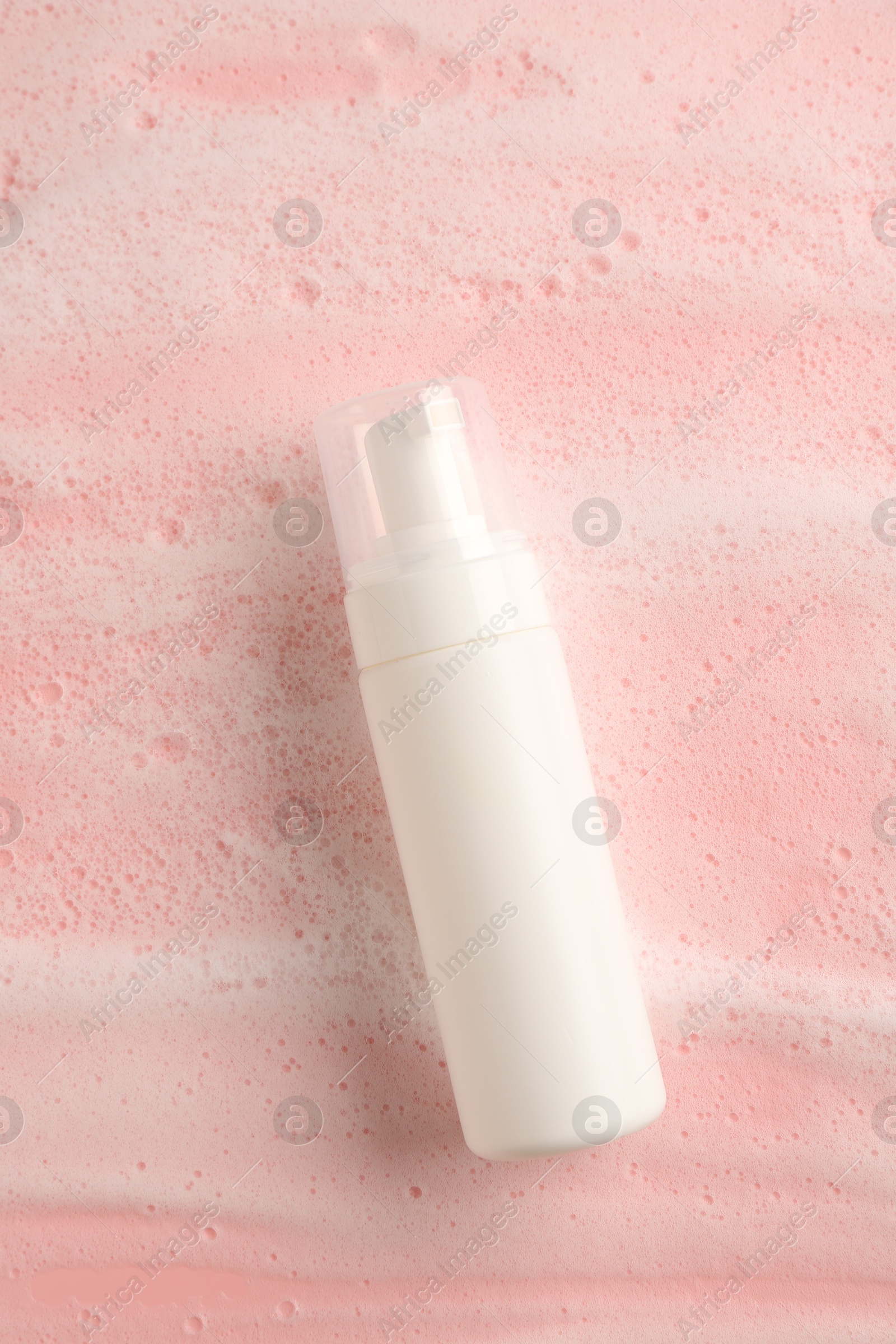 Photo of Bottle of cosmetic product with foam on pink background, top view