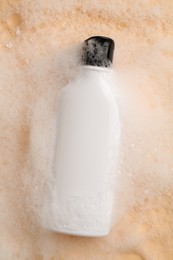 Bottle of cosmetic product with foam on beige background, top view