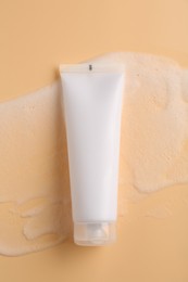 Photo of Tube of cosmetic product with foam on beige background, top view