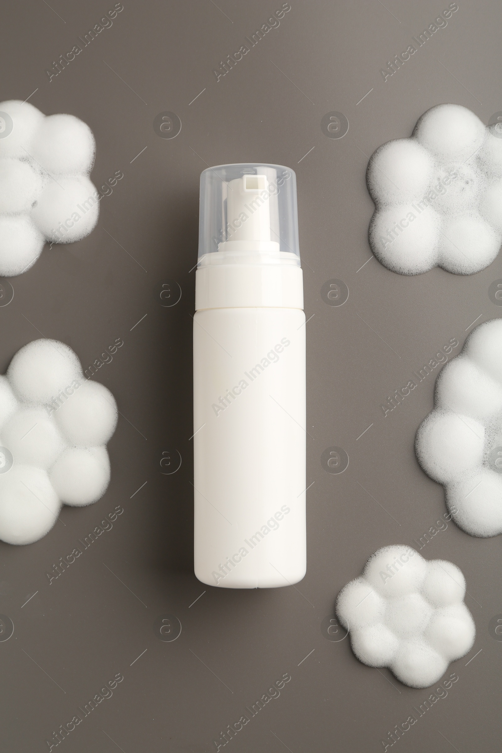 Photo of Bottle of cosmetic product with foam in shape of flowers on grey background, top view