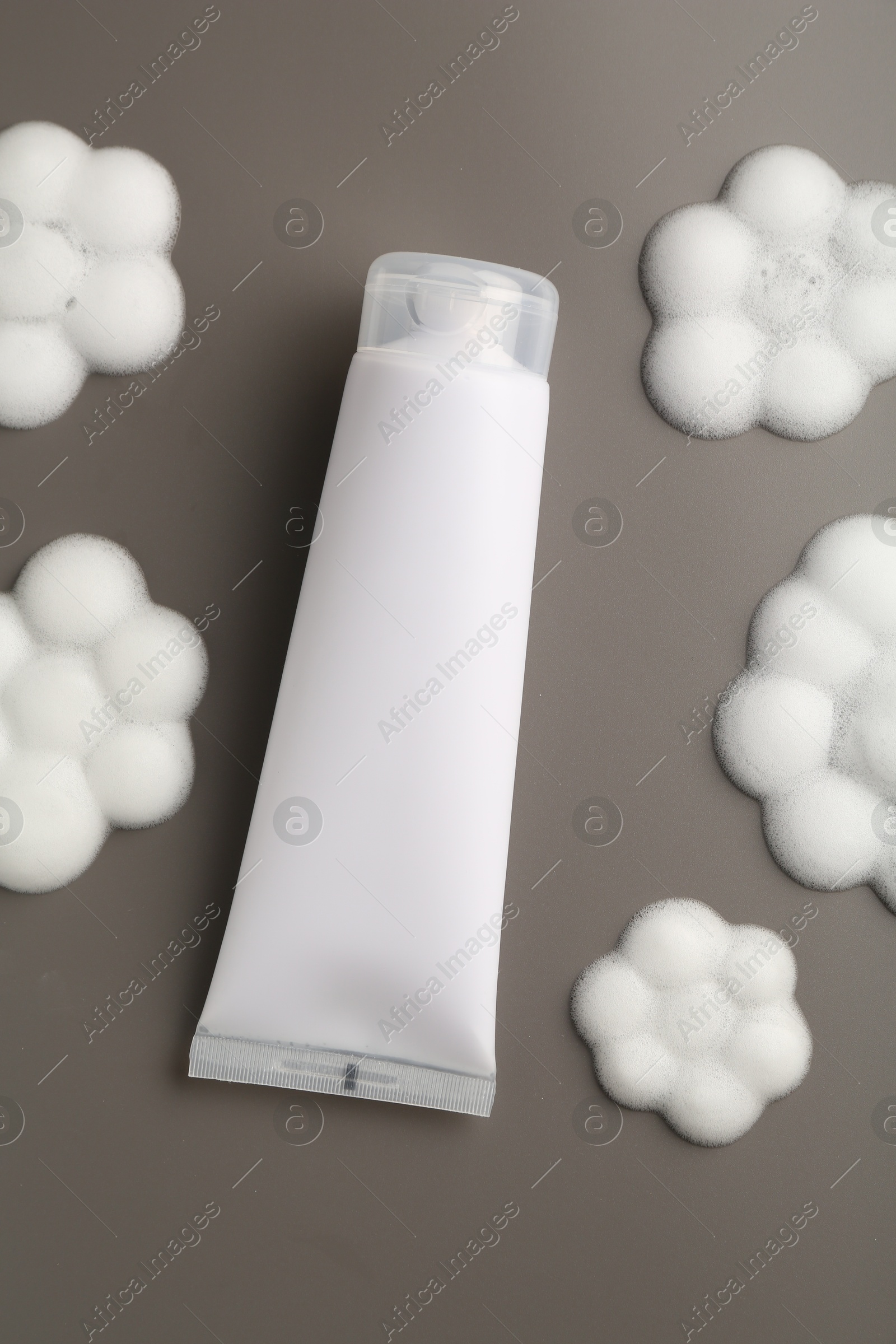 Photo of Tube of cosmetic product with foam in shape of flowers on grey background, top view