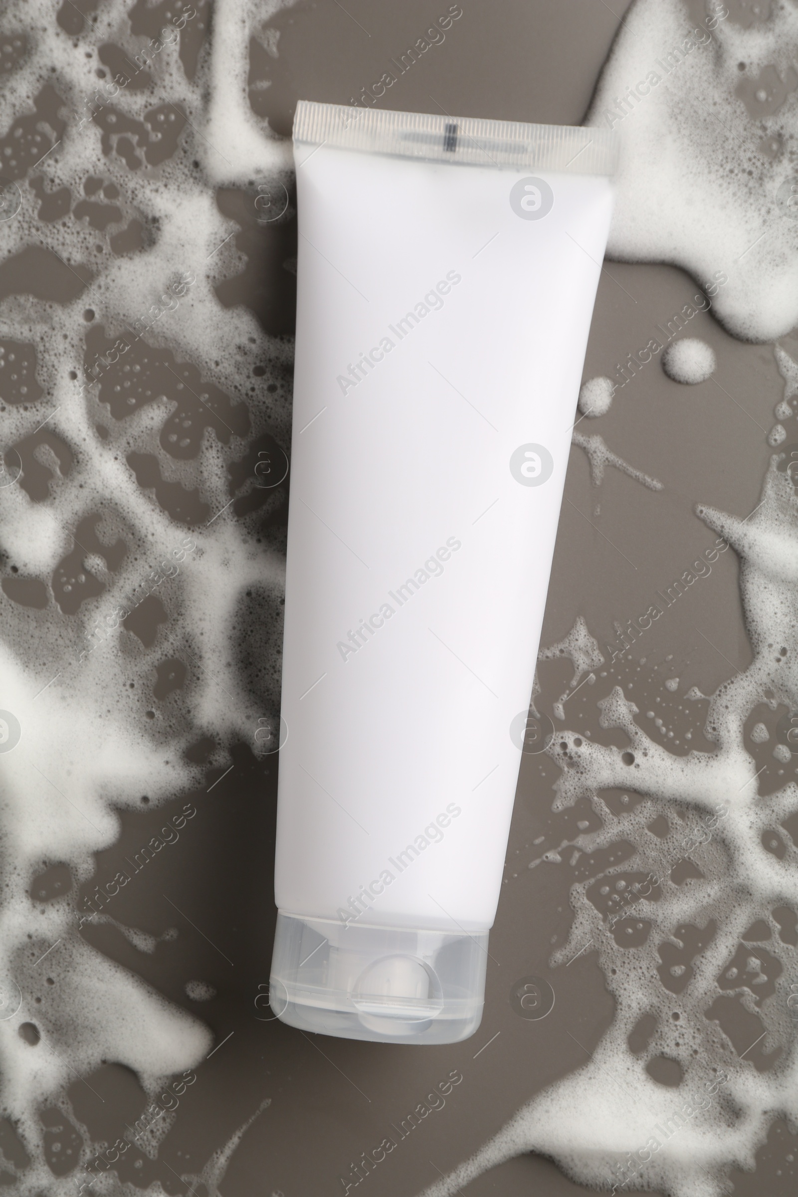 Photo of Tube of cosmetic product with foam on grey background, top view