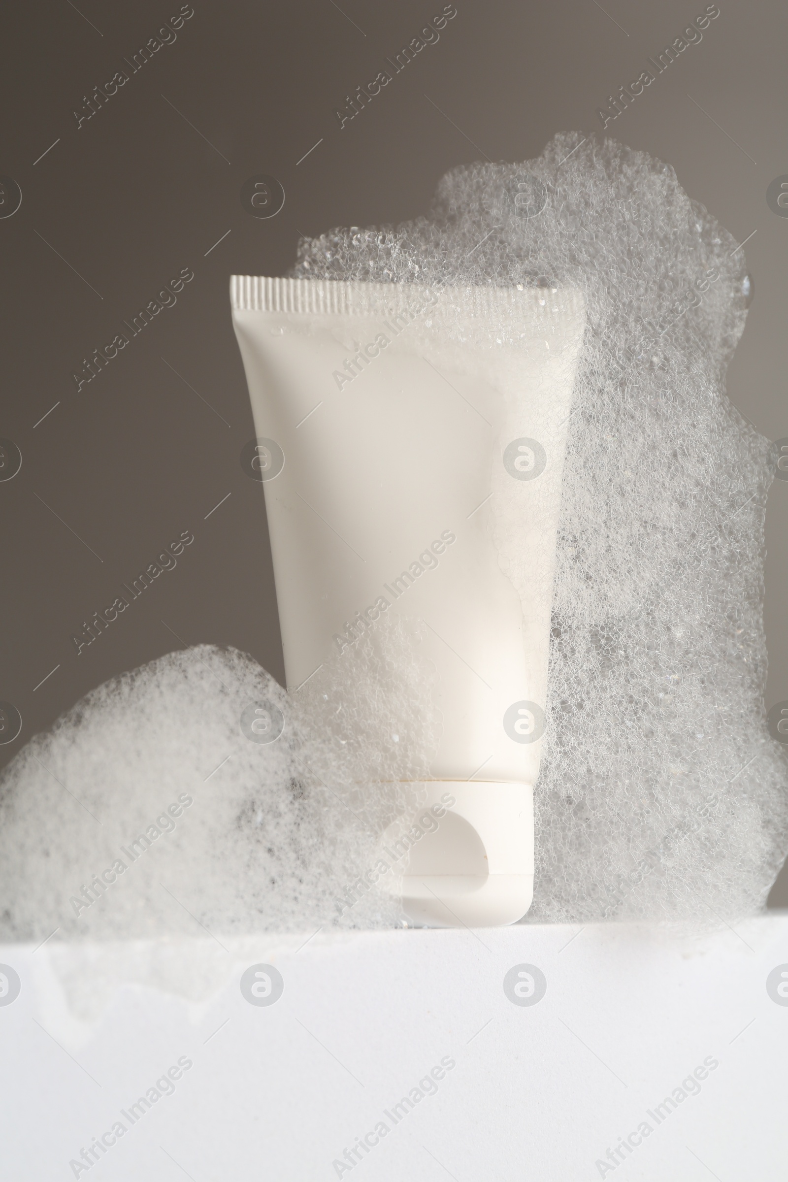 Photo of Tube of cosmetic product with foam on white surface against grey background