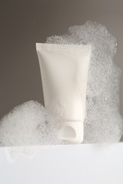 Photo of Tube of cosmetic product with foam on white surface against grey background