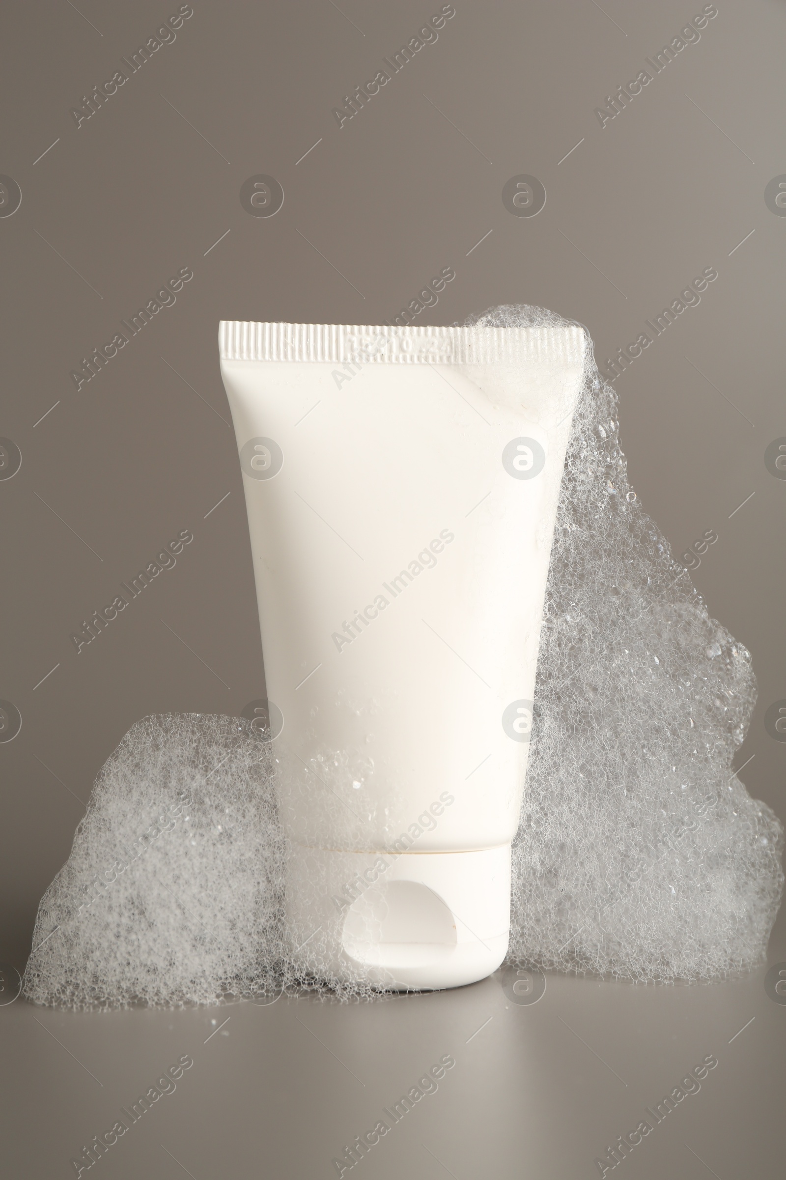 Photo of Tube of cosmetic product with foam on grey background