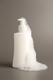 Bottle of cosmetic product with foam on grey background