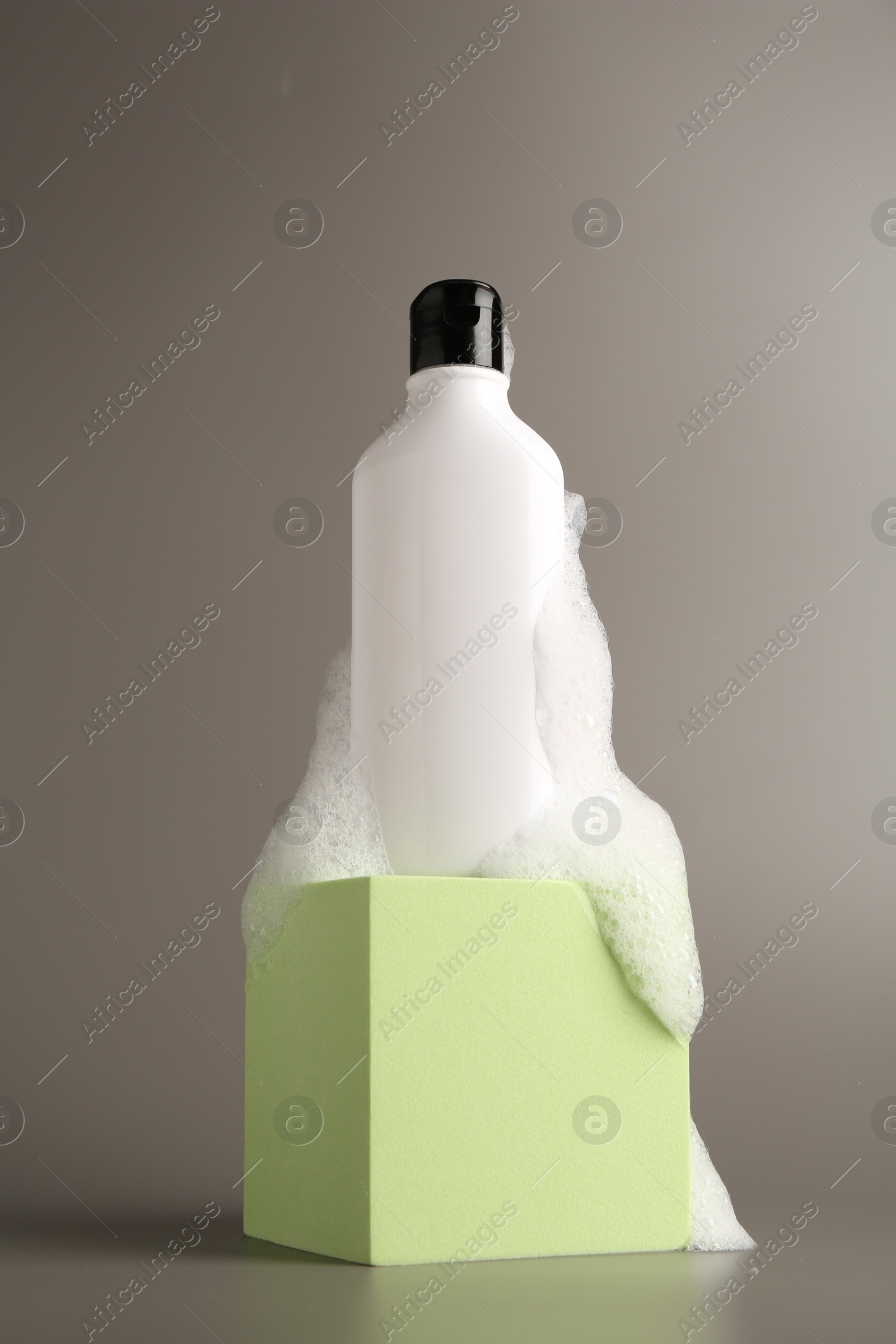 Photo of Bottle of cosmetic product with foam on podium against grey background