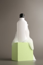 Photo of Bottle of cosmetic product with foam on podium against grey background