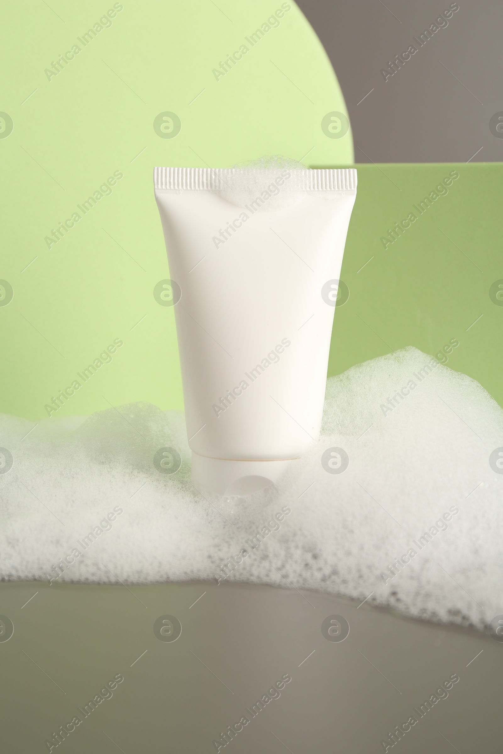 Photo of Presentation of cosmetic product in tube with foam on grey background, closeup