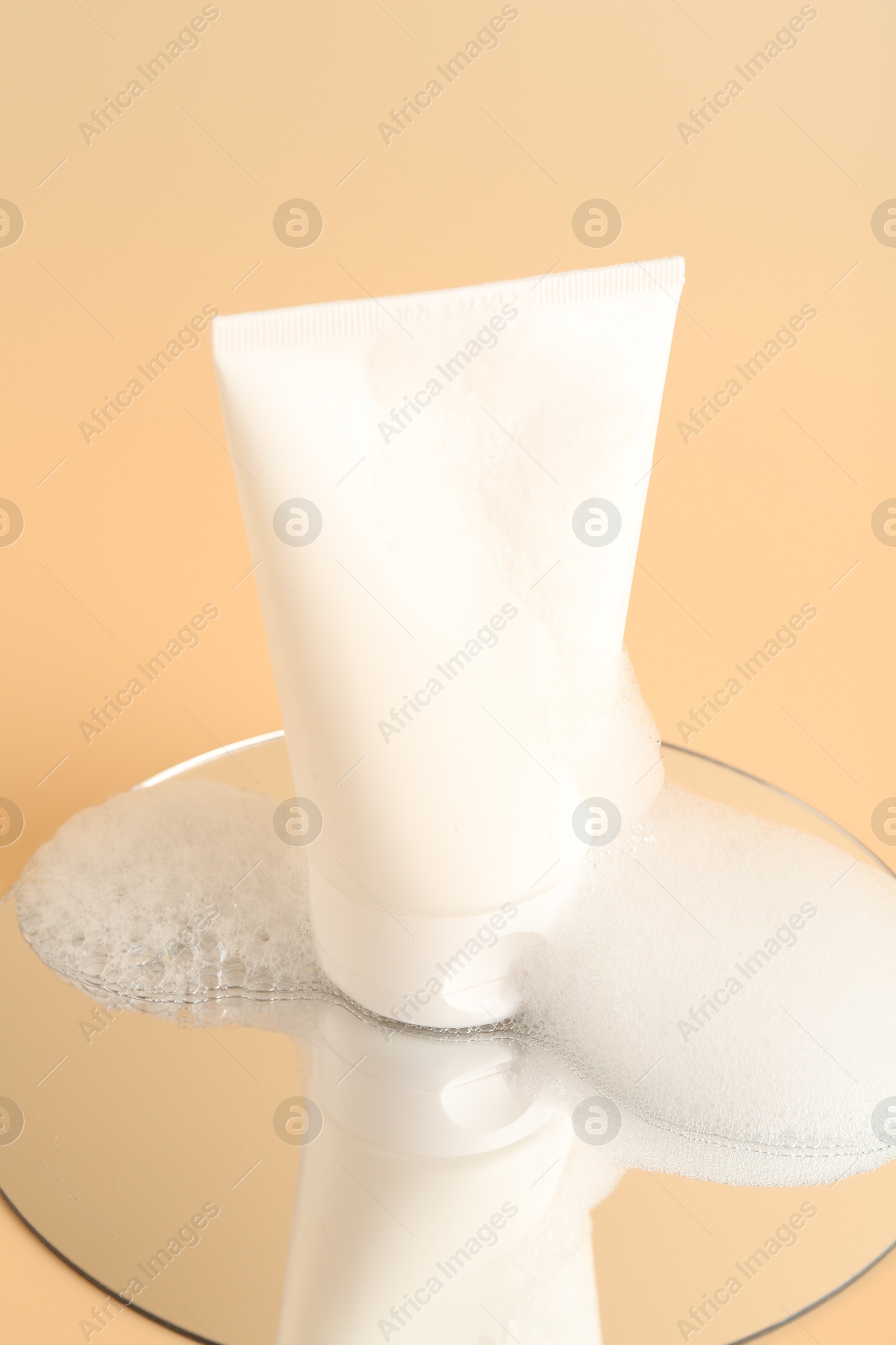 Photo of Tube of cosmetic product with foam and mirror on beige background