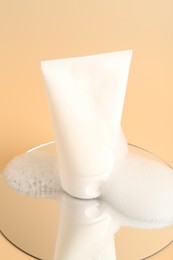 Photo of Tube of cosmetic product with foam and mirror on beige background