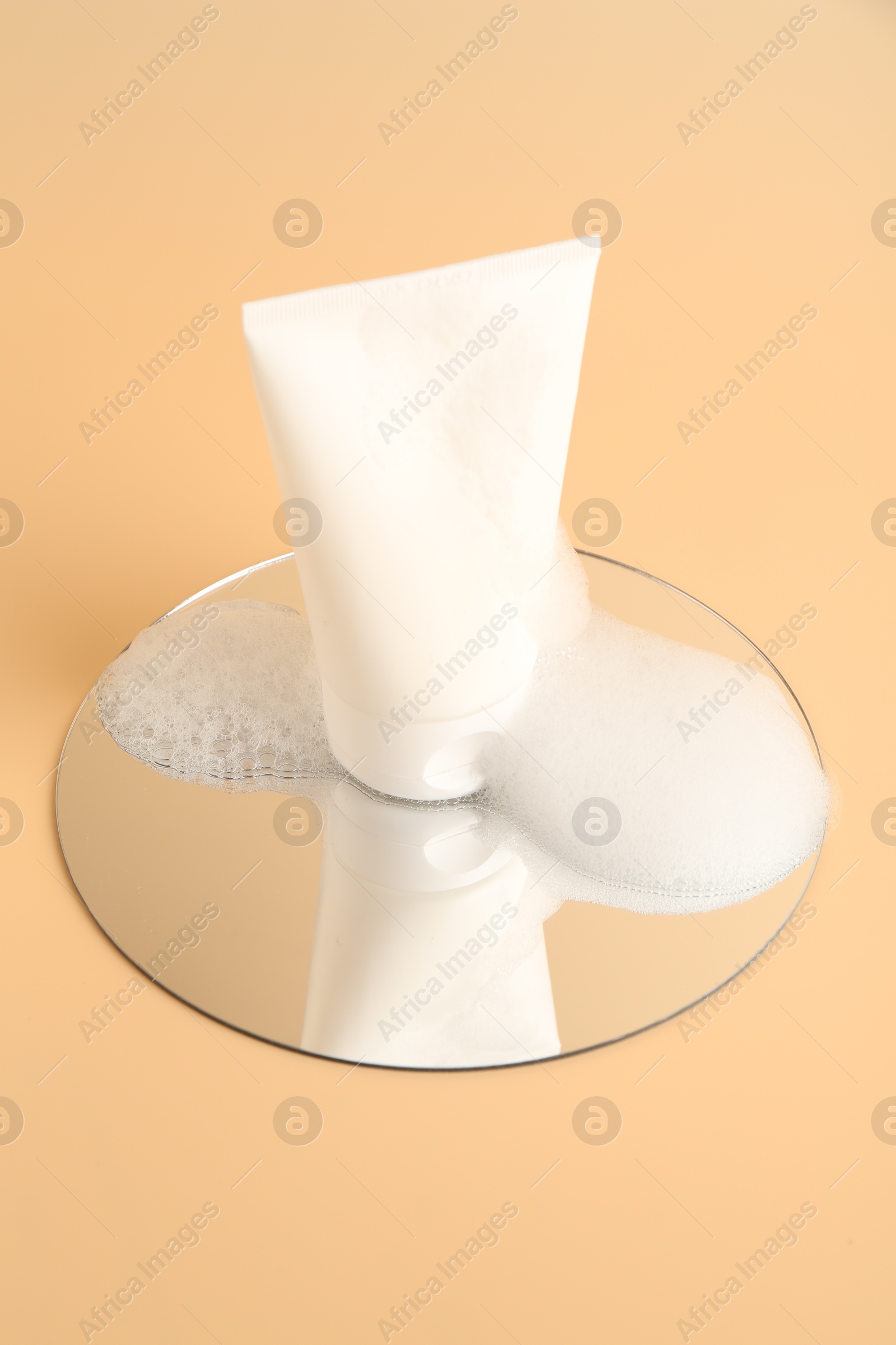 Photo of Tube of cosmetic product with foam and mirror on beige background