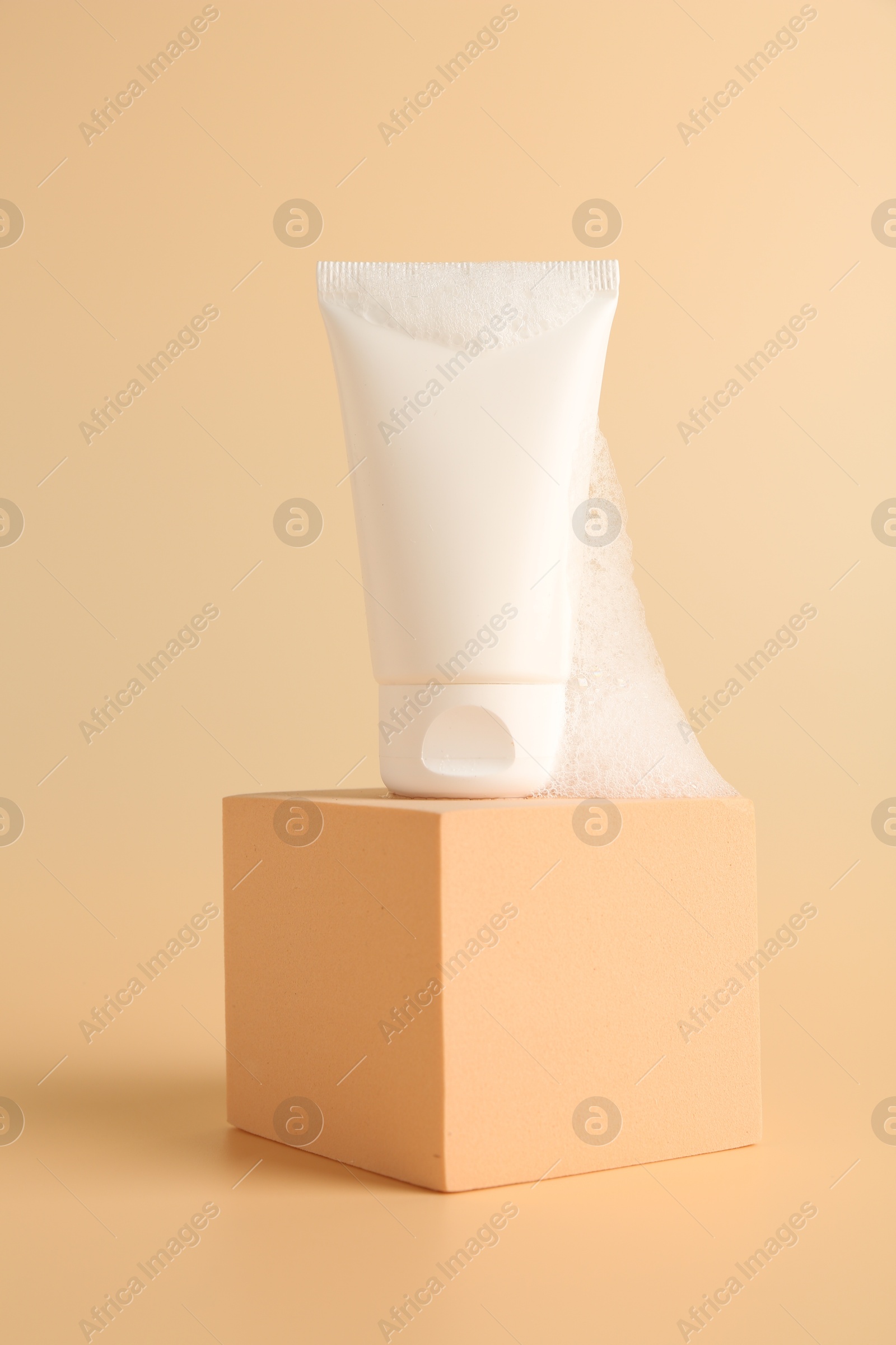 Photo of Tube of cosmetic product with foam on podium against beige background