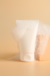 Photo of Tube of cosmetic product with foam and podium on beige background