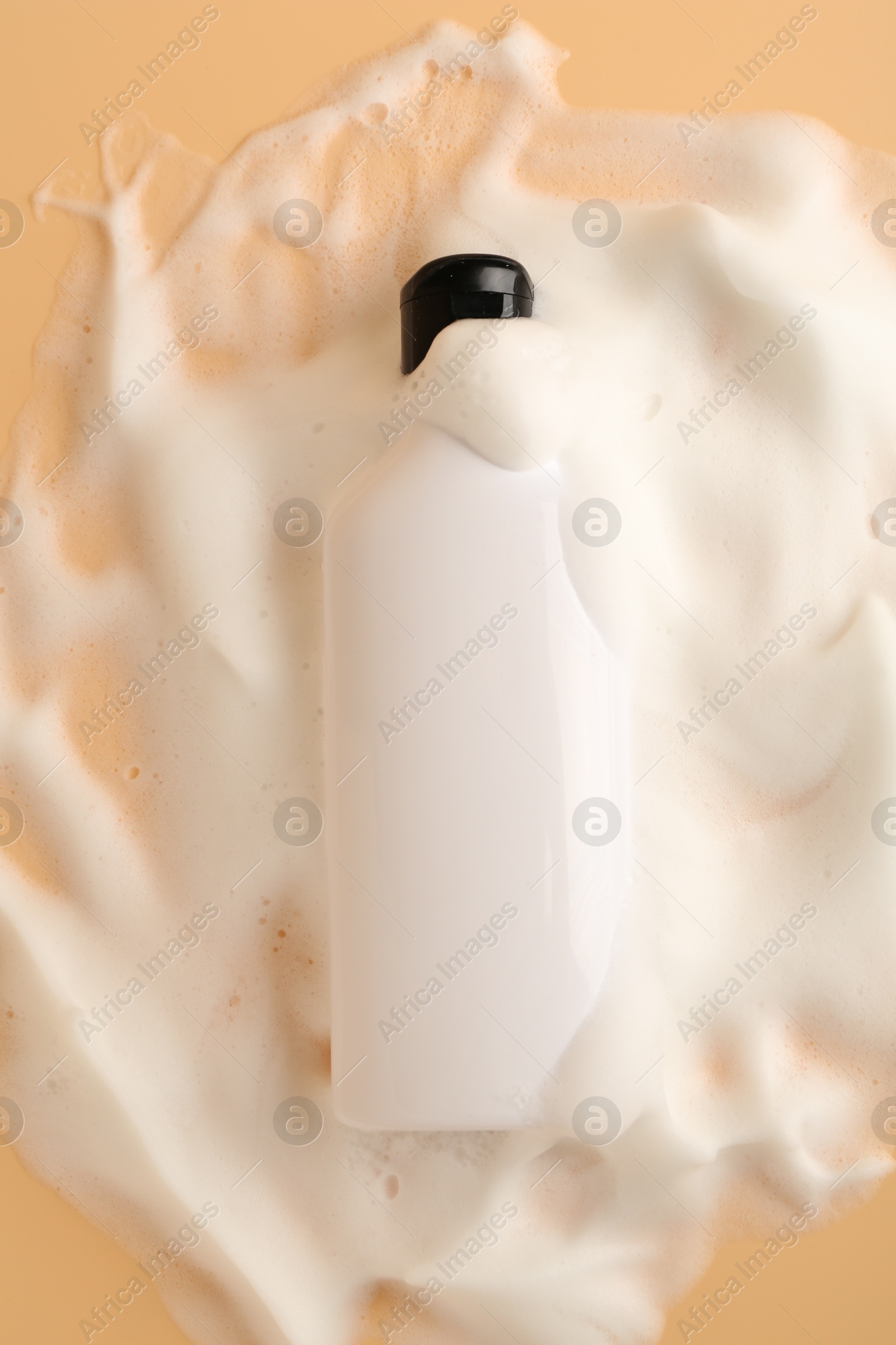 Photo of Bottle of cosmetic product with foam on beige background, top view