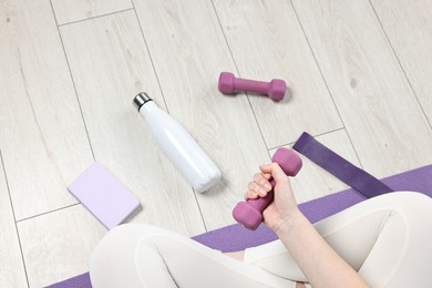 Photo of Woman with dumbbell, thermo bottle and planner on floor indoors, above view