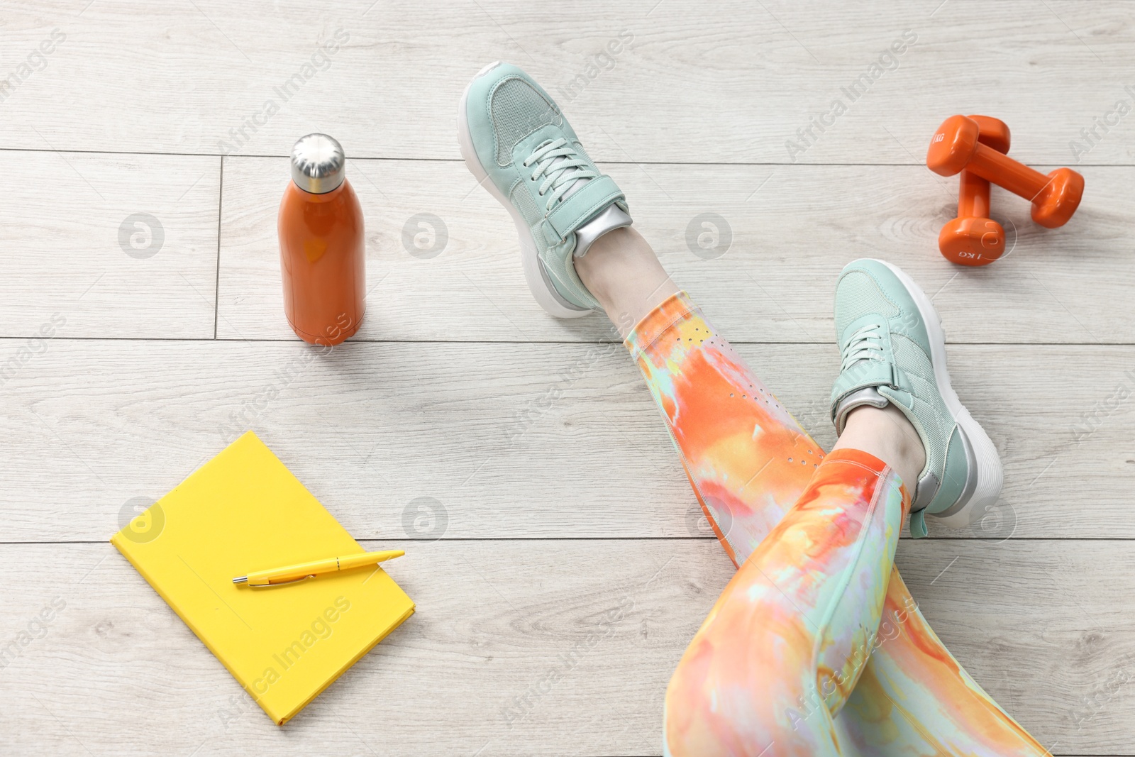 Photo of Woman with gym equipment and planner on floor indoors, above view