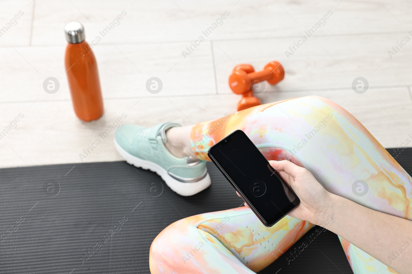 Photo of Woman with smartphone and gym equipment on floor indoors, closeup