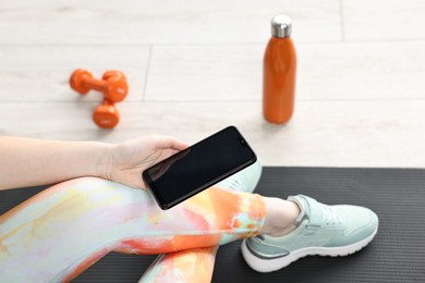 Woman with smartphone and gym equipment on floor indoors, closeup