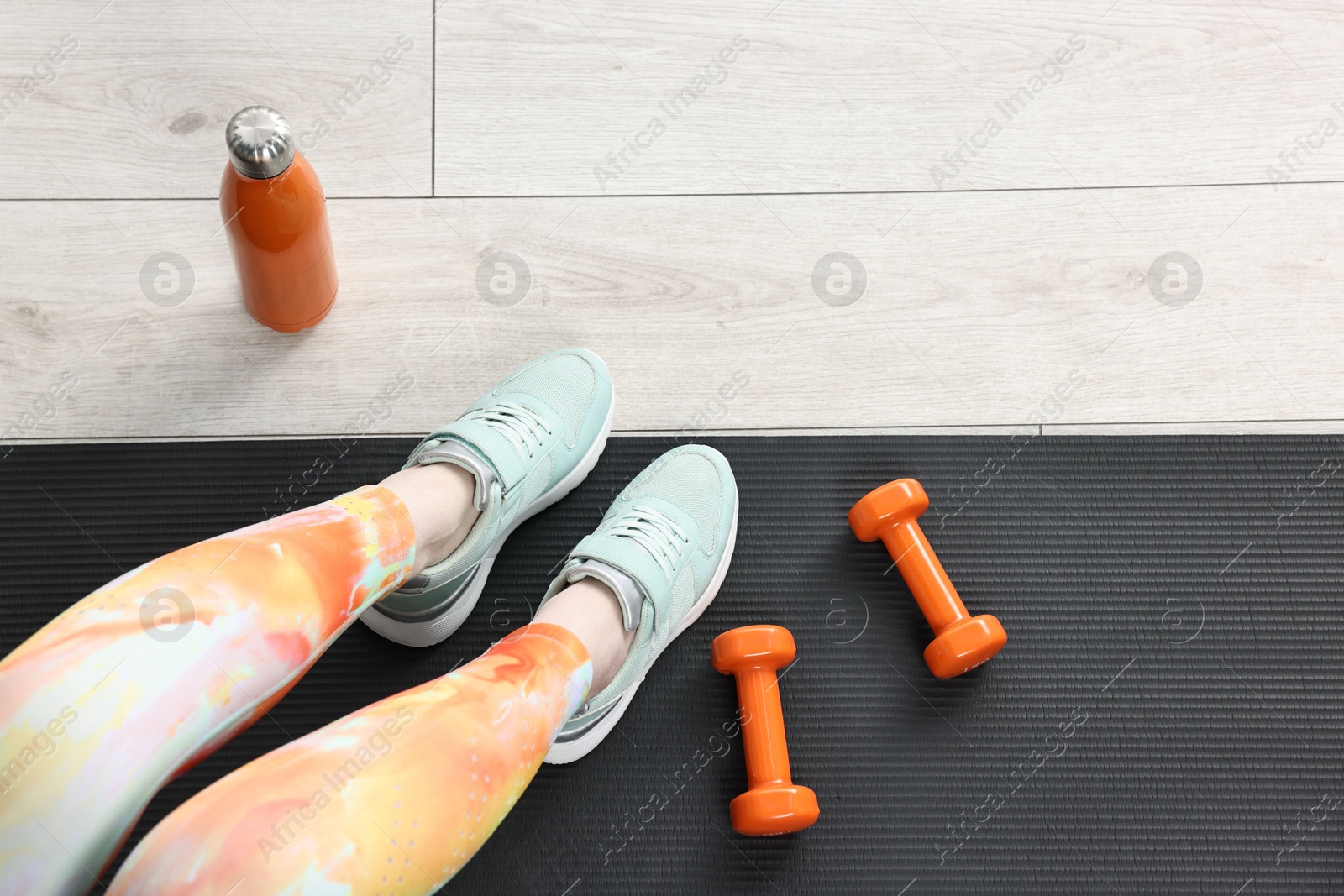 Photo of Woman with dumbbells and thermo bottle on floor indoors, top view