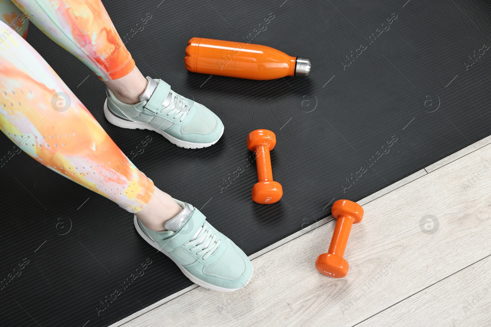 Photo of Woman with dumbbells and thermo bottle on floor indoors, above view