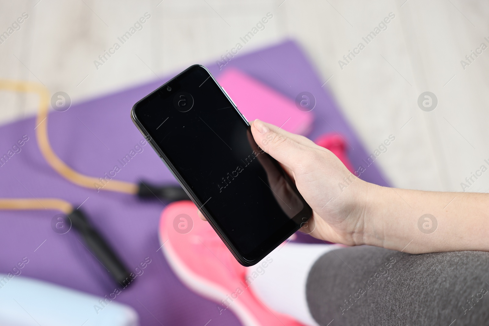 Photo of Woman with smartphone and gym equipment on floor indoors, closeup