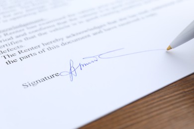 Photo of Ballpoint pen leaving signature on contract at wooden table, closeup