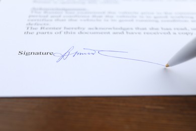 Photo of Ballpoint pen leaving signature on contract at wooden table, closeup