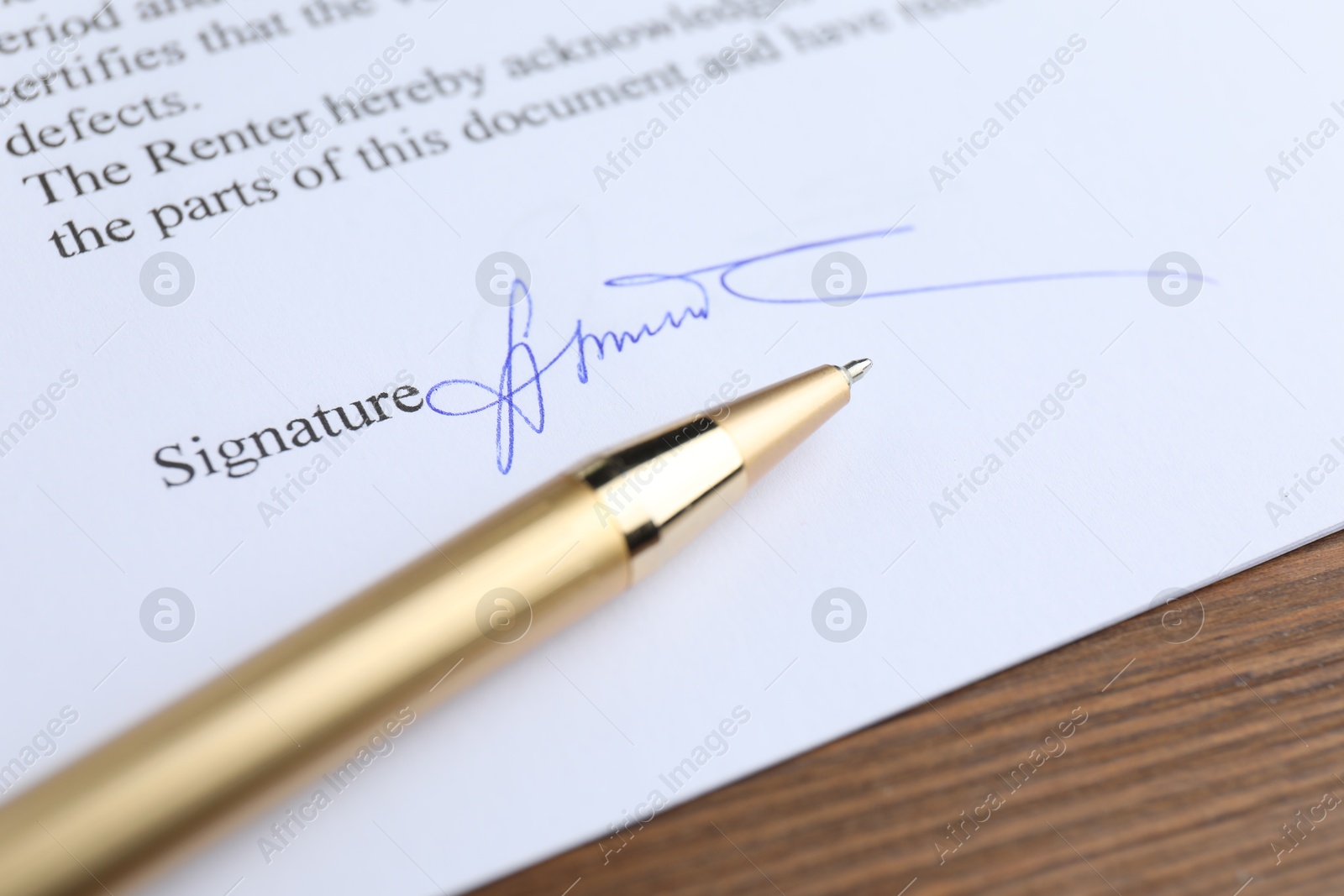 Photo of Ballpoint pen and signature on contract at wooden table, closeup