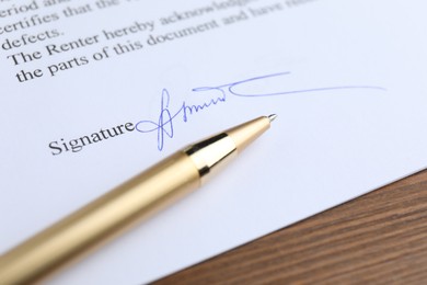 Photo of Ballpoint pen and signature on contract at wooden table, closeup