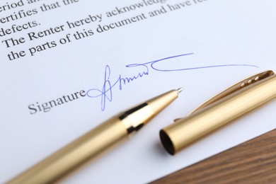 Photo of Ballpoint pen and signature on contract at wooden table, closeup