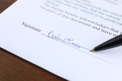 Photo of Ballpoint pen leaving signature on contract at wooden table, closeup