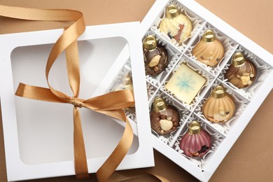 Photo of Open box with delicious chocolate in shape of Christmas ornaments on beige background, top view