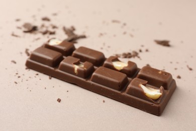 Photo of Tasty chocolate bar and crumbs on beige background, closeup