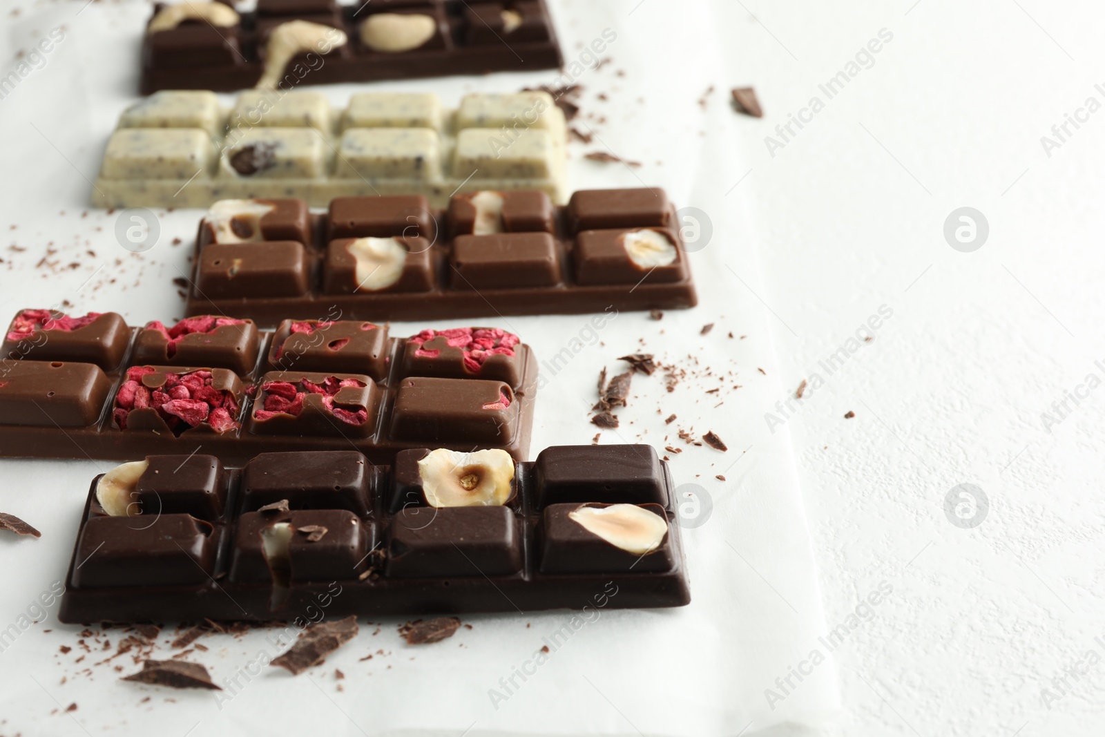 Photo of Tasty chocolate bars and crumbs on white textured background, closeup. Space for text