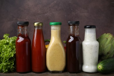 Photo of Tasty sauces in glass bottles and fresh products on wooden table, closeup