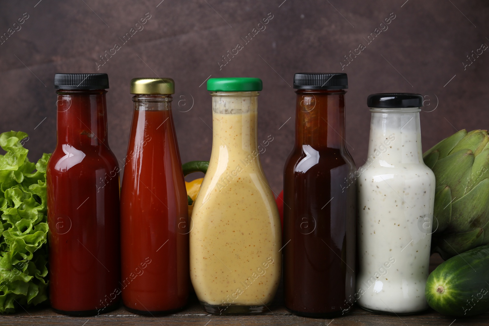 Photo of Tasty sauces in glass bottles and fresh products on wooden table, closeup