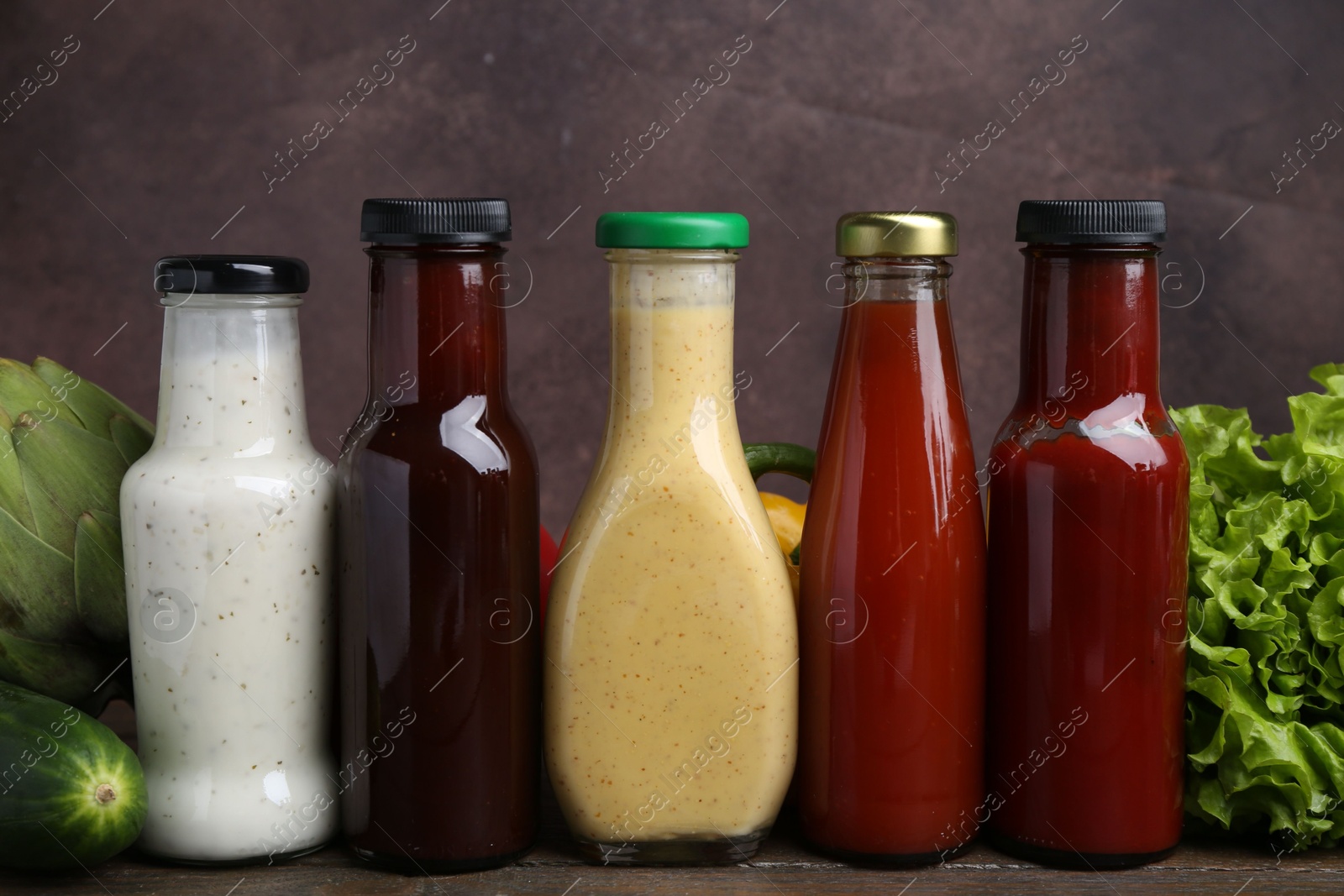 Photo of Tasty sauces in glass bottles and fresh products on wooden table, closeup