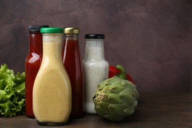 Photo of Tasty sauces in glass bottles and fresh products on wooden table, closeup. Space for text