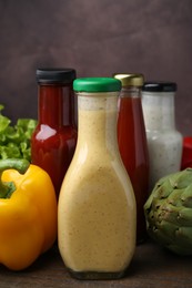 Photo of Tasty sauces in glass bottles and fresh products on wooden table, closeup