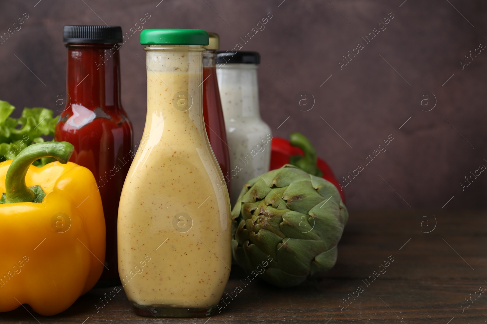 Photo of Tasty sauces in glass bottles and fresh products on wooden table, closeup. Space for text