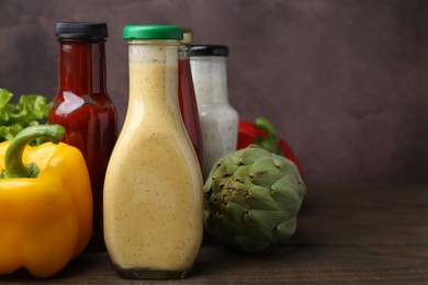 Photo of Tasty sauces in glass bottles and fresh products on wooden table, closeup. Space for text