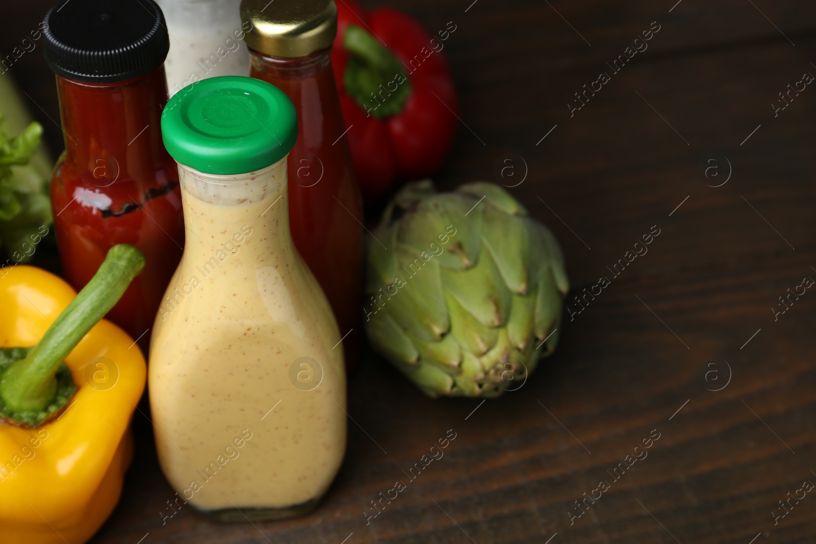 Photo of Tasty sauces in glass bottles and fresh products on wooden table, closeup. Space for text