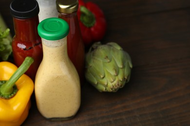 Photo of Tasty sauces in glass bottles and fresh products on wooden table, closeup. Space for text