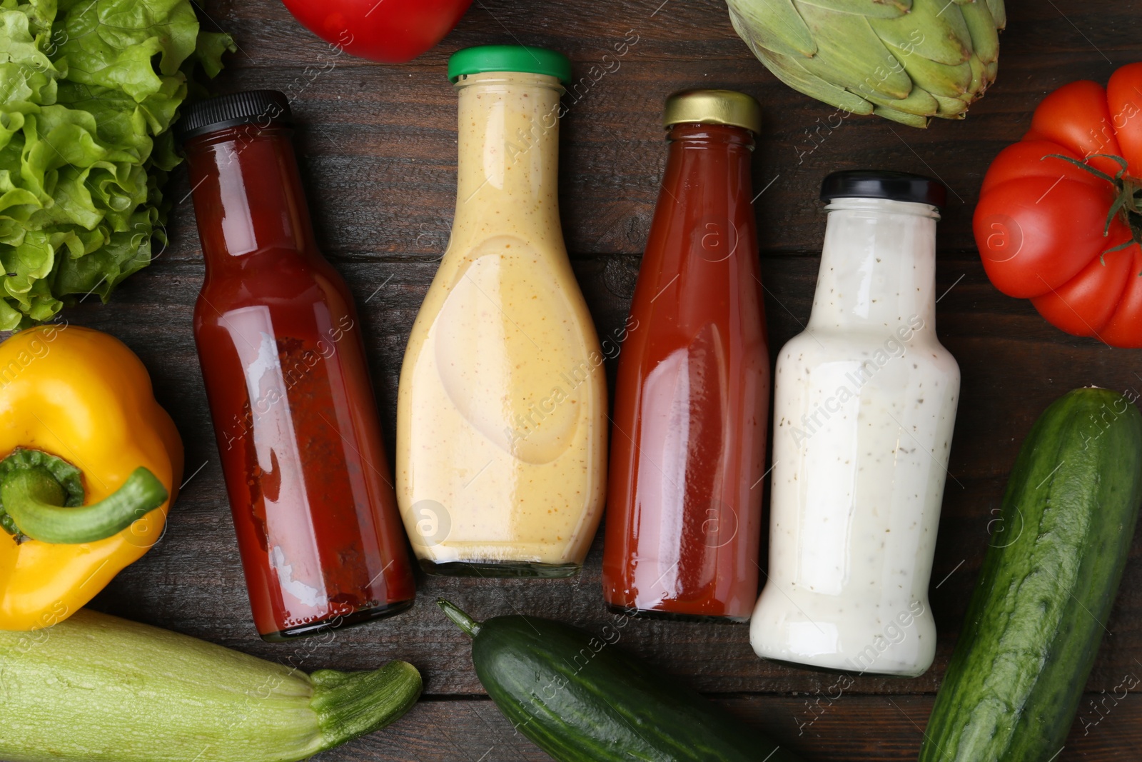 Photo of Tasty sauces in glass bottles and fresh products on wooden table, flat lay