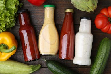 Photo of Tasty sauces in glass bottles and fresh products on wooden table, flat lay